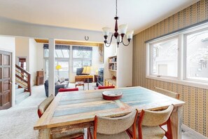 A dining area with a wooden table, wicker chairs, a chandelier, and a view through a window. - Light-filled, dog-friendly home with fireplace & great location near skiing/golf (Avon)