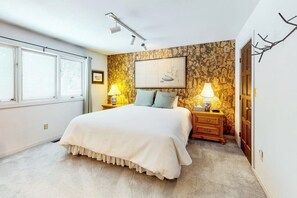 A bedroom with a large bed, two bedside tables with lamps, a stone-patterned wall, a framed picture, and a window with blinds. - Light-filled, dog-friendly home with fireplace & great location near skiing/golf (Avon)