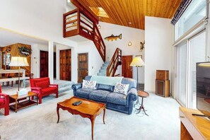 A spacious living area with a blue sofa, red chairs, a wooden coffee table, and a staircase with wooden railings. - Light-filled, dog-friendly home with fireplace & great location near skiing/golf (Avon)