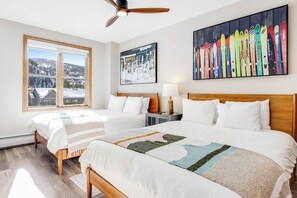 Ein Hotelzimmer mit zwei Betten, einem großen Fenster mit Ausblick, einem Deckenventilator und einer Wand mit einer farbenfrohen Ausstellung von Ski-Ausrüstung.