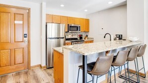 A modern kitchen with wooden cabinets, stainless steel appliances, and a bar area with stools. - Second-story condo with mountain view, fireplace & balcony - walk to gondola (Avon)