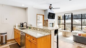 A modern kitchen with granite countertops, wooden cabinets, a dishwasher, and a ceiling fan. - Second-story condo with mountain view, fireplace & balcony - walk to gondola (Avon)