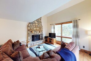 Ein Wohnzimmer mit Kamin aus Stein, einem Fernseher, einer Couch und einem großen Fenster.