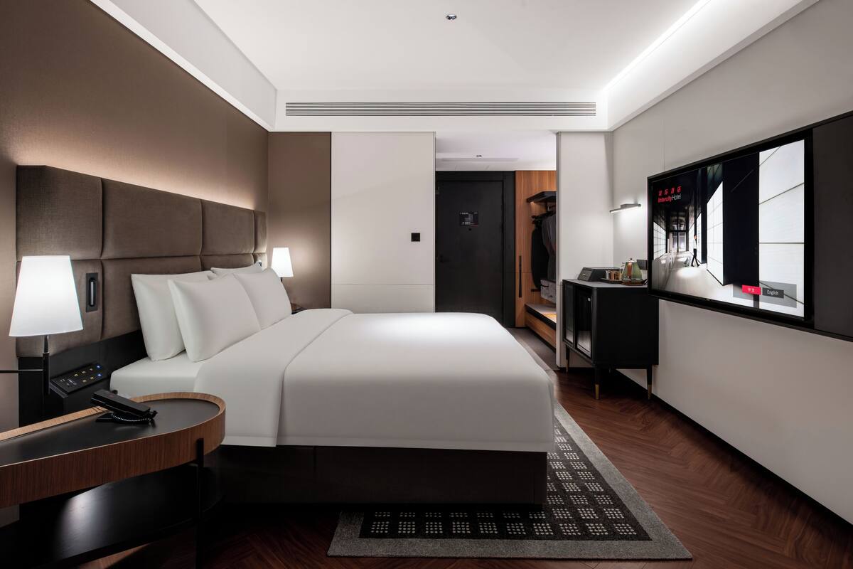A modern hotel room with a large bed, bedside tables, a desk, and a large mirror.