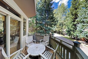 Ein Balkon mit Tisch und Stühlen, umgeben von Bäumen und wolkenlosem Himmel.