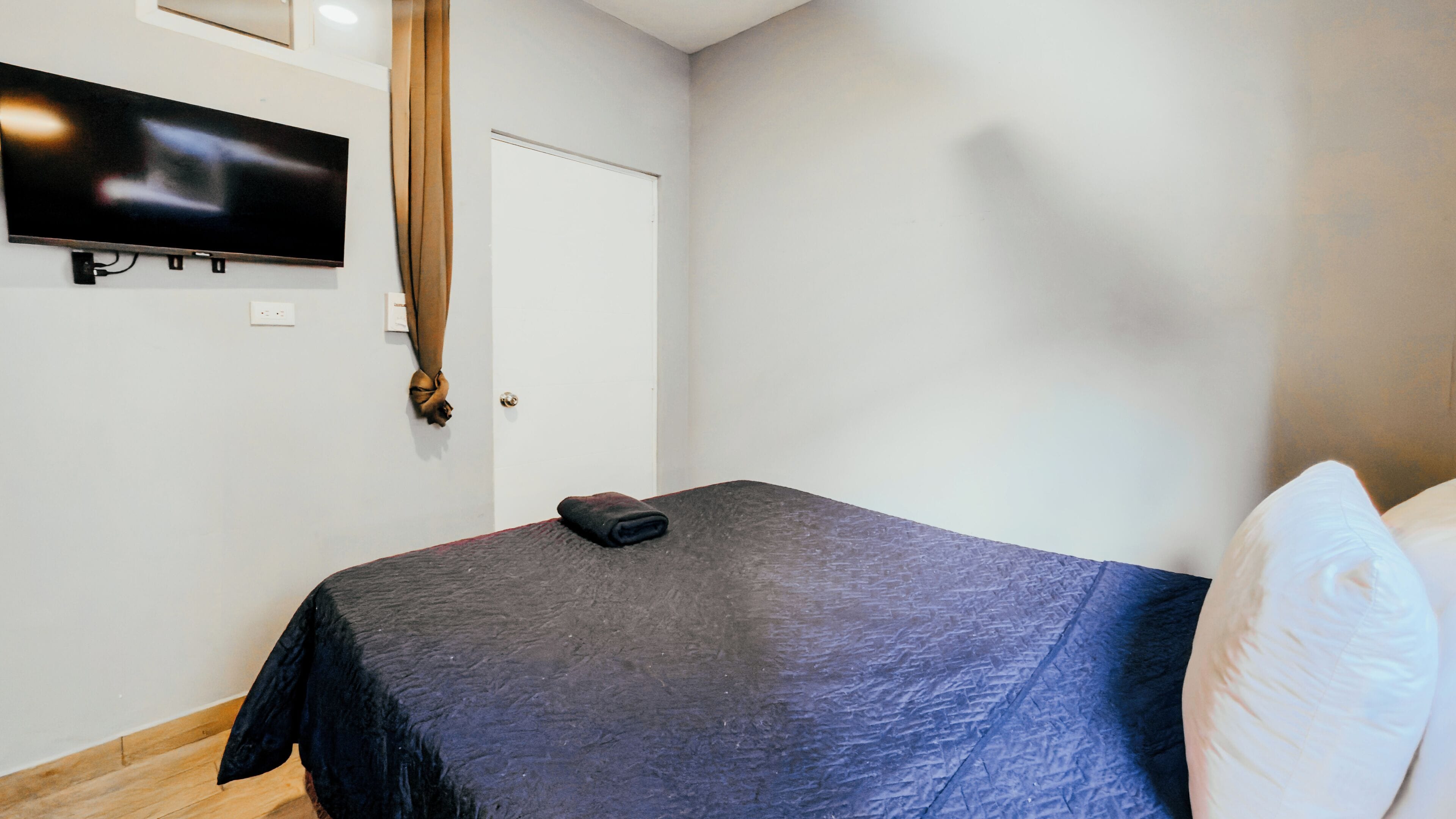 Un dormitorio con una cama, televisión montada en la pared y una puerta.
