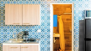 A kitchen with patterned wallpaper, wooden cabinets, a sink, a coffee maker, and a shower area. - Villa Verona (Guatemala City)