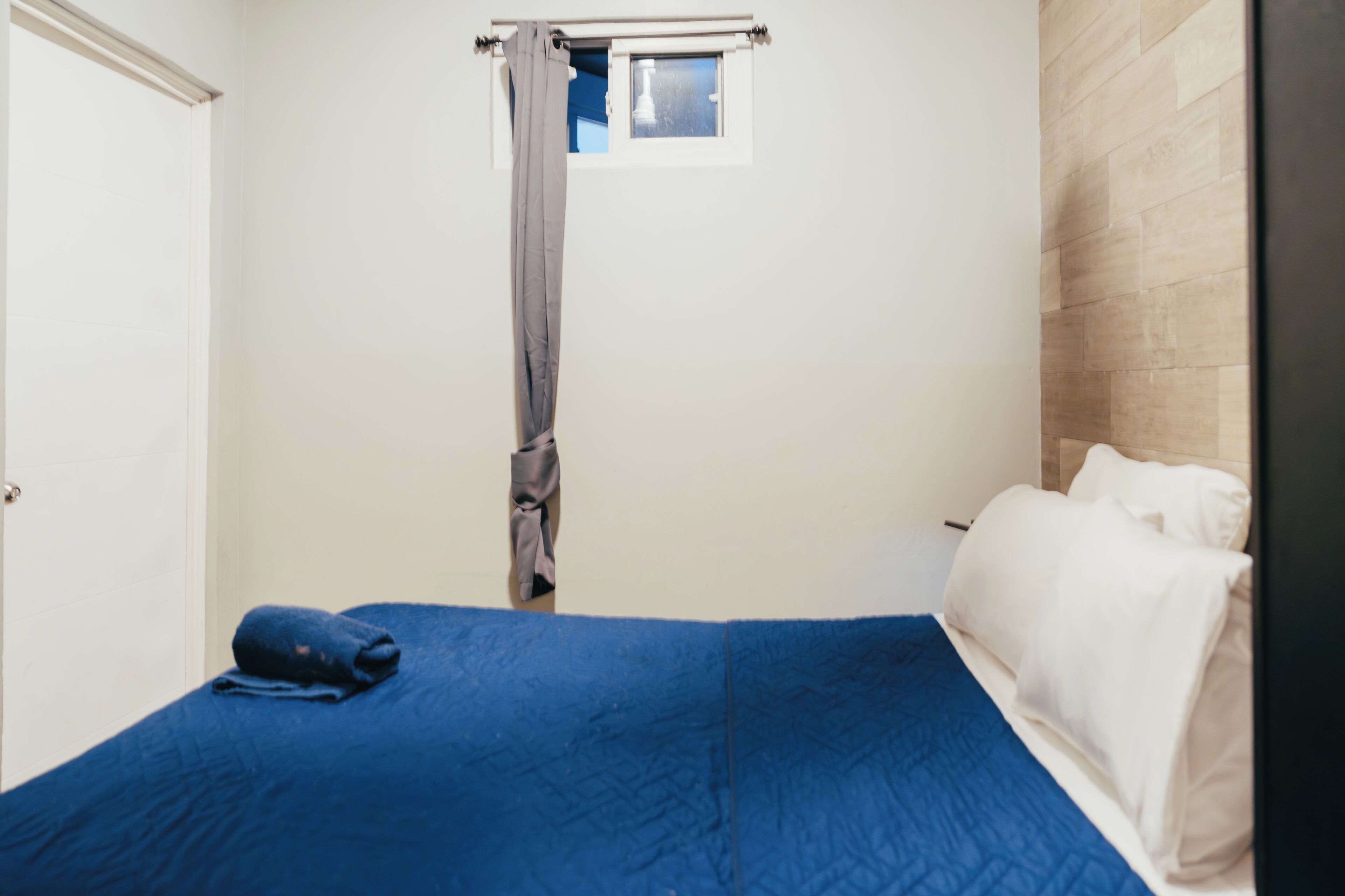 Une pièce avec un lit, une fenêtre avec un rideau et une porte.