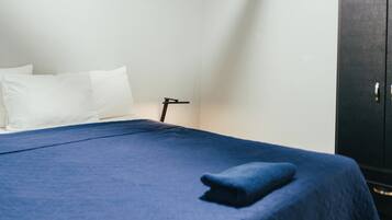 A bed with a blue bedspread, white pillows, and a black nightstand with a lamp.