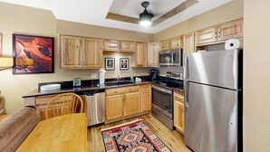 A kitchen with wooden cabinets, stainless steel appliances, a ceiling fan, and a dining area with a table and chairs. - Mountain getaway near trails & skiing w/ balcony &  shared amenities (Avon)