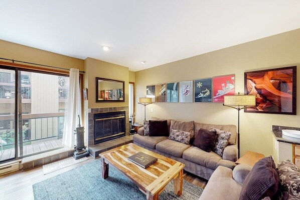 A living room with a sofa, coffee table, fireplace, and artwork on the wall. - Mountain getaway near trails & skiing w/ balcony & shared amenities (Avon)
