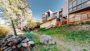 A modern building with a staircase leading to a balcony, surrounded by trees and a pile of logs. - Mountain getaway near trails & skiing w/ balcony &  shared amenities (Avon)