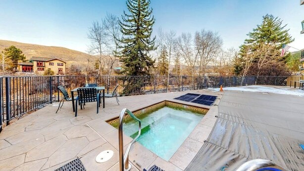 A swimming pool with a metal ladder, surrounded by a fence, with a chair and table nearby. - Mountain getaway near trails & skiing w/ balcony &  shared amenities (Avon)