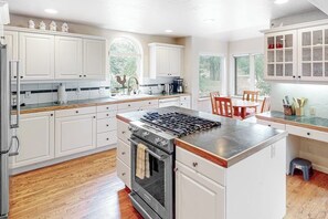 A kitchen with white cabinets, a stainless steel stove, wooden countertops, and a dining area with chairs. - Friendly Home with Gas Fireplace, High-Speed WiFi, & Central AC (Avon)