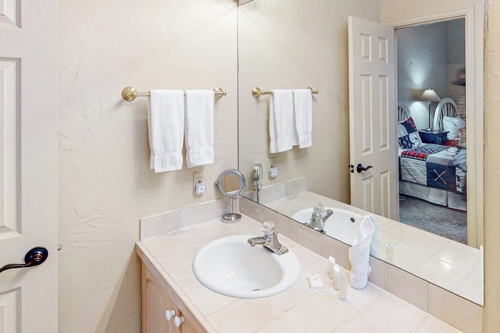 A bathroom with a sink, mirror, towel rack, and a door leading to a bedroom.