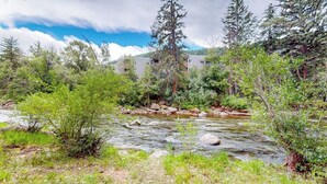 Ein Fluss fließt durch eine natürliche Landschaft mit Bäumen und einem Gebäude im Hintergrund.