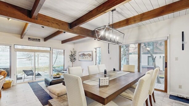 A spacious dining area with a wooden table and white chairs, large windows, and a view of the outdoors. - Stylishly Remodeled Mountain Retreat on Eagle Vail Golf Course (Avon)