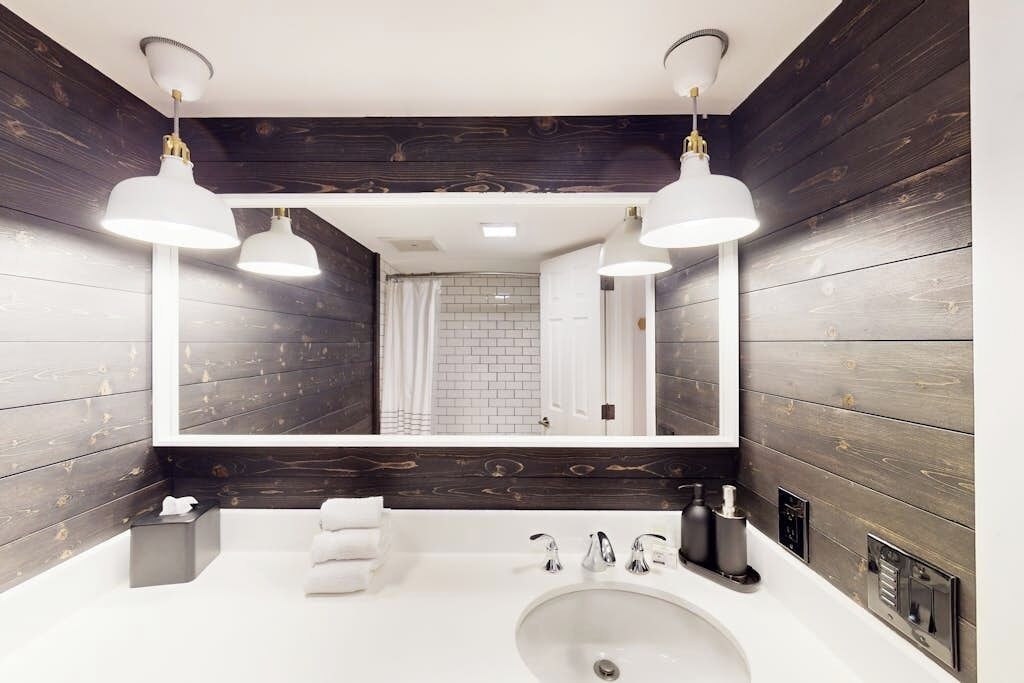 Une salle de bain moderne avec un grand miroir, un lavabo blanc et deux lampes suspendues.