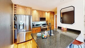 A kitchen with wooden cabinets, stainless steel appliances, a granite countertop, and a black backsplash. - Cozy, recently remodeled condo with patio, mountain views & W/D - near slopes (Avon)