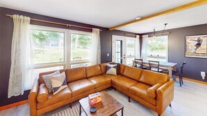 A living room with a brown leather sofa, a wooden coffee table, and a dining area with a table and chairs. - Cozy, recently remodeled condo with patio, mountain views & W/D - near slopes (Avon)
