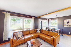 Ein Wohnzimmer mit braunem Ledersofa, einem Holztisch und einem Essbereich mit Tisch und Stühlen.