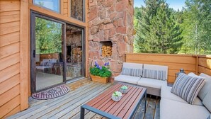 Une terrasse en bois avec un muret en pierre, un canapé et une table agrémentée d’objets décoratifs.