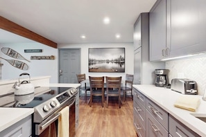 A modern kitchen with a stove, oven, and dining area with chairs. - Lovely condo with fireplace, mountain view, full kitchen, & skiing nearby (Avon)