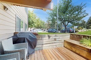 A wooden deck with a covered seating area, a view of a parking lot, and a residential building in the background. - Lovely condo with fireplace, mountain view, full kitchen, & skiing nearby (Avon)