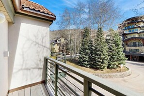 A balcony with a railing, a snow-covered tree, and a building in the background. - Luxury ski in ski out condo w/ fast wifi, ski locker & great location (Mountain Village)