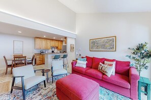 Ein modernes Wohnzimmer mit einem roten Sofa, einem Couchtisch und einem Essbereich mit Holzsesseln. Im Hintergrund ist eine Küche zu sehen.