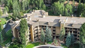 A multi-story hotel with a central courtyard, surrounded by trees and other buildings. - Cozy condo with amazing mountain view, pool & hot tub - next to golf/Nordic ski (Vail)