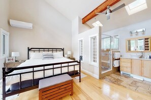 Ein Schlafzimmer mit Bett, Nachttisch, Sitzbank und einem Badezimmer mit Waschbecken und Spiegel.
