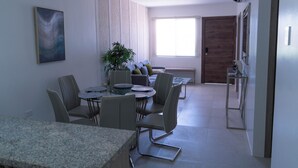 Een moderne woonkamer met een bank, een eethoek met stoelen en een tafel, een groot raam en een deur.