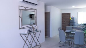Een moderne keuken met een inbouwoven, een eethoek met een glazen tafel en metalen stoelen, en een wandmodel airconditioner.