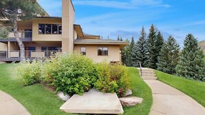 A modern two-story house with a well-maintained lawn, a stone pathway leading to the entrance, and a backdrop of evergreen trees. - Mountain view condo with large balcony, pool & hot tub - steps to ski shuttle (Vail)