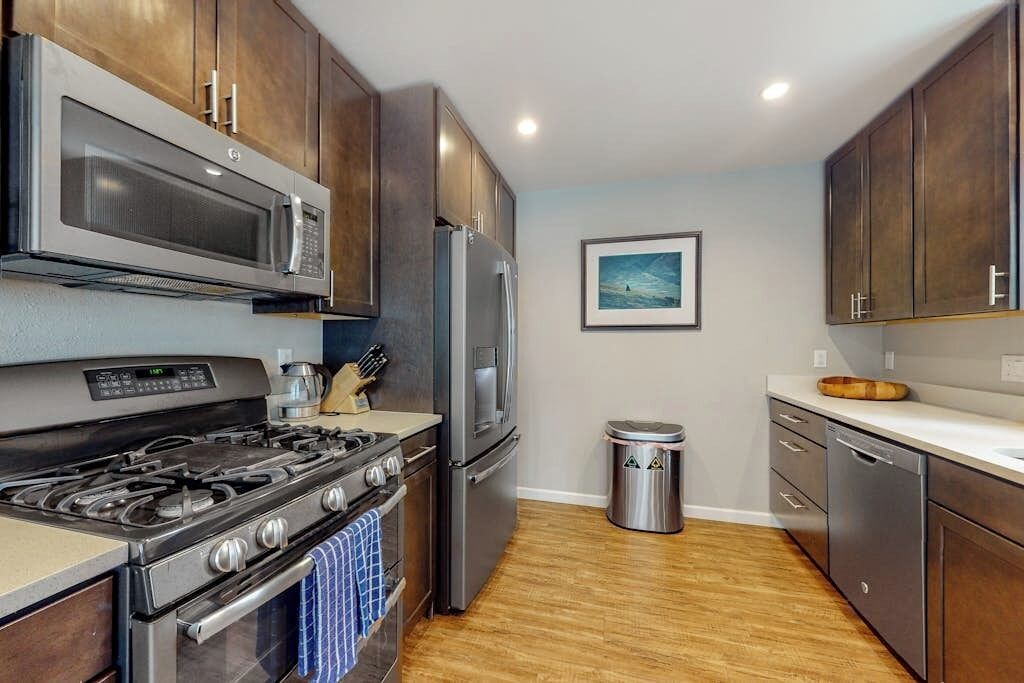 A kitchen with stainless steel appliances, wooden cabinets, and a trash can.