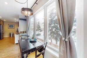 Ein Essbereich mit Tisch, Stühlen, einer Chandelierleuchtre und Blick auf verschneite Bäume durch große Fenster.