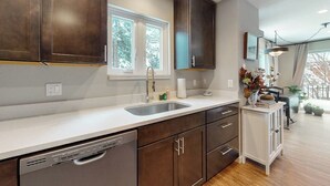Een moderne keuken met donkere kastjes, een wit aanrecht, een inbouwvaatwasser en een raam dat voor natuurlijk licht zorgt.