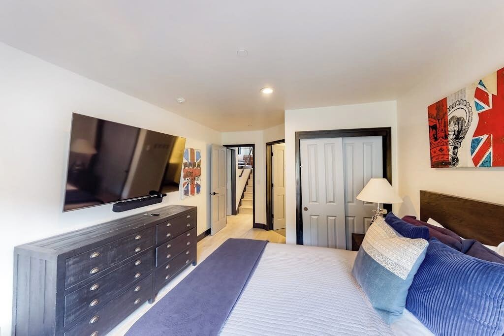 Un dormitorio con cama, cómoda, televisión y obras de arte en la pared.