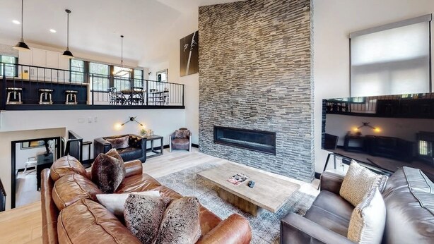 Una sala de estar moderna con chimenea, sofás de cuero y un comedor con techos altos.