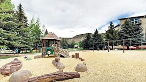 Ein Spielplatz mit einer Holzspielanlage, Sandboden und umliegenden Bäumen.