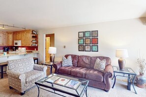 Ein Wohnzimmer mit braunem Ledersofa, einem gemusterten Sessel und einem Glastisch.