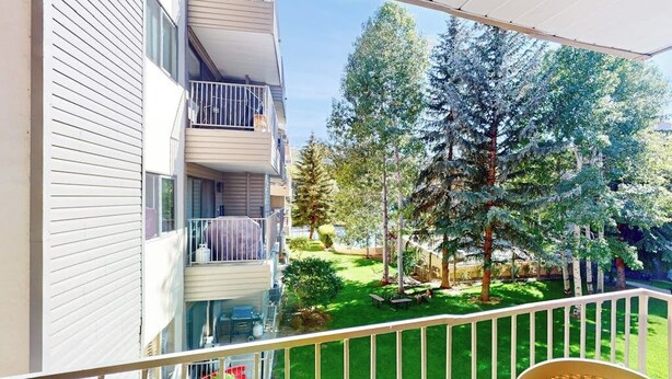 Ein Balkon mit Blick auf eine grüne Rasenfläche und Bäume, einem weißen Geländer und einem Korbstuhl.