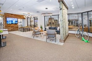 Ein moderner Büroarbeitsplatz mit einer Wandpaneele aus Holz, einem Fernseher, einer Sitzecke mit Stühlen und Sofas sowie einem Fahrrad.
