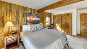 Un dormitorio con una cama grande, paredes de madera, un techo con vigas a la vista, una mesita de noche con lámpara y un cuadro sobre la cama.