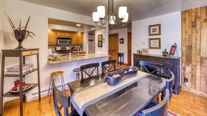 Una cocina moderna con armarios de madera, una isla central y un comedor con una mesa y sillas oscuras.