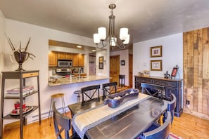A modern kitchen with wooden cabinets, a central island, and a dining area with a dark table and chairs. - Upscale condo on shuttle route to Vail w/ a full kitchen, shared pool & tennis (East Vail)