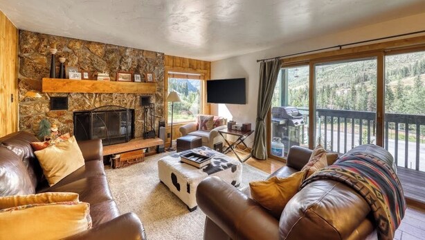 Una sala de estar acogedora con chimenea de piedra, sofás de cuero, televisor de pantalla plana y grandes ventanales con vistas al exterior.