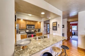 A kitchen with granite countertops, wooden cabinets, stainless steel appliances, and a bar stool area. - Upscale condo on shuttle route to Vail w/ a full kitchen, shared pool & tennis (East Vail)
