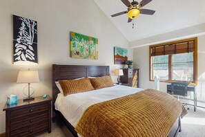 A bedroom with a bed, nightstand, lamp, ceiling fan, artwork, window, and desk. - Conveniently located condo with kitchen, fast wifi & balcony & mountain views (Avon)